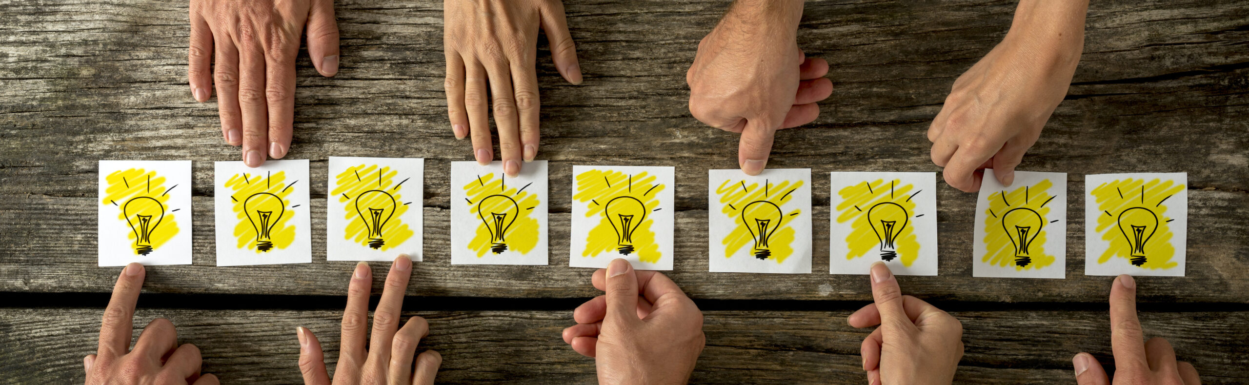 Brainstorming and teamwork concept with a group of diverse business people each holding out a card with a shining light bulb arranged in a row conceptual of ideas, inspiration and innovation.